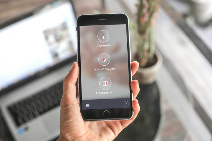 Smartphone in Hand mit sichtbarem Bildschirm, der drei Anwendungen zeigt: Ged&auml;chtnistrainer, Anruf-Assistent, Erinnerungbuch.