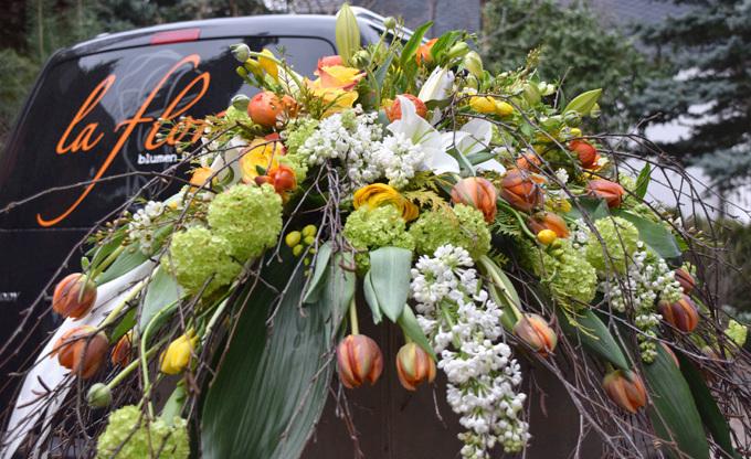 Blumenarrangement aus Tulpen, Lilien und anderen Blumen, dekorativ auf einem Fahrzeug montiert.