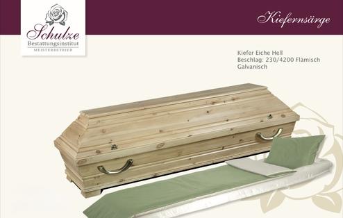 Holzbestattungsurne aus heller Kiefer mit grünem Kissen auf einer weißen Matratze, vor neutralem Hintergrund.