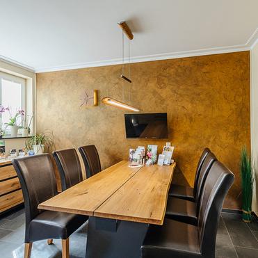 Essbereich mit einem großen Holz-Tisch und schwarzen Stühlen, dekoriert mit Pflanzen und moderner Beleuchtung an der Wand.
